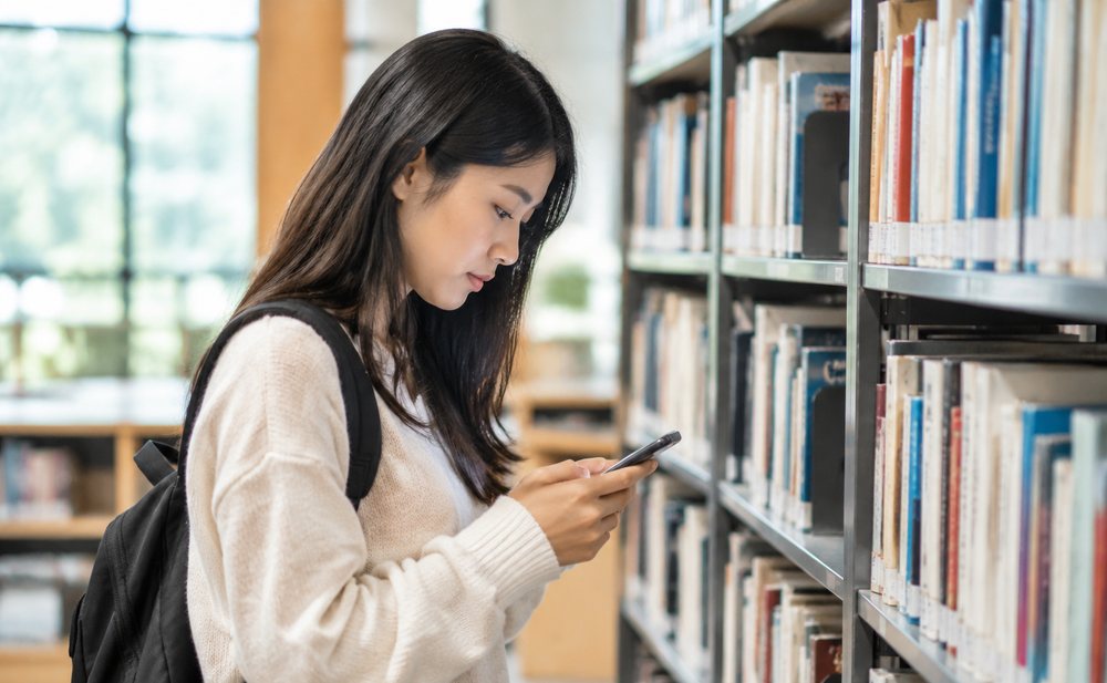 图书馆书架前的读者用手机查阅资料